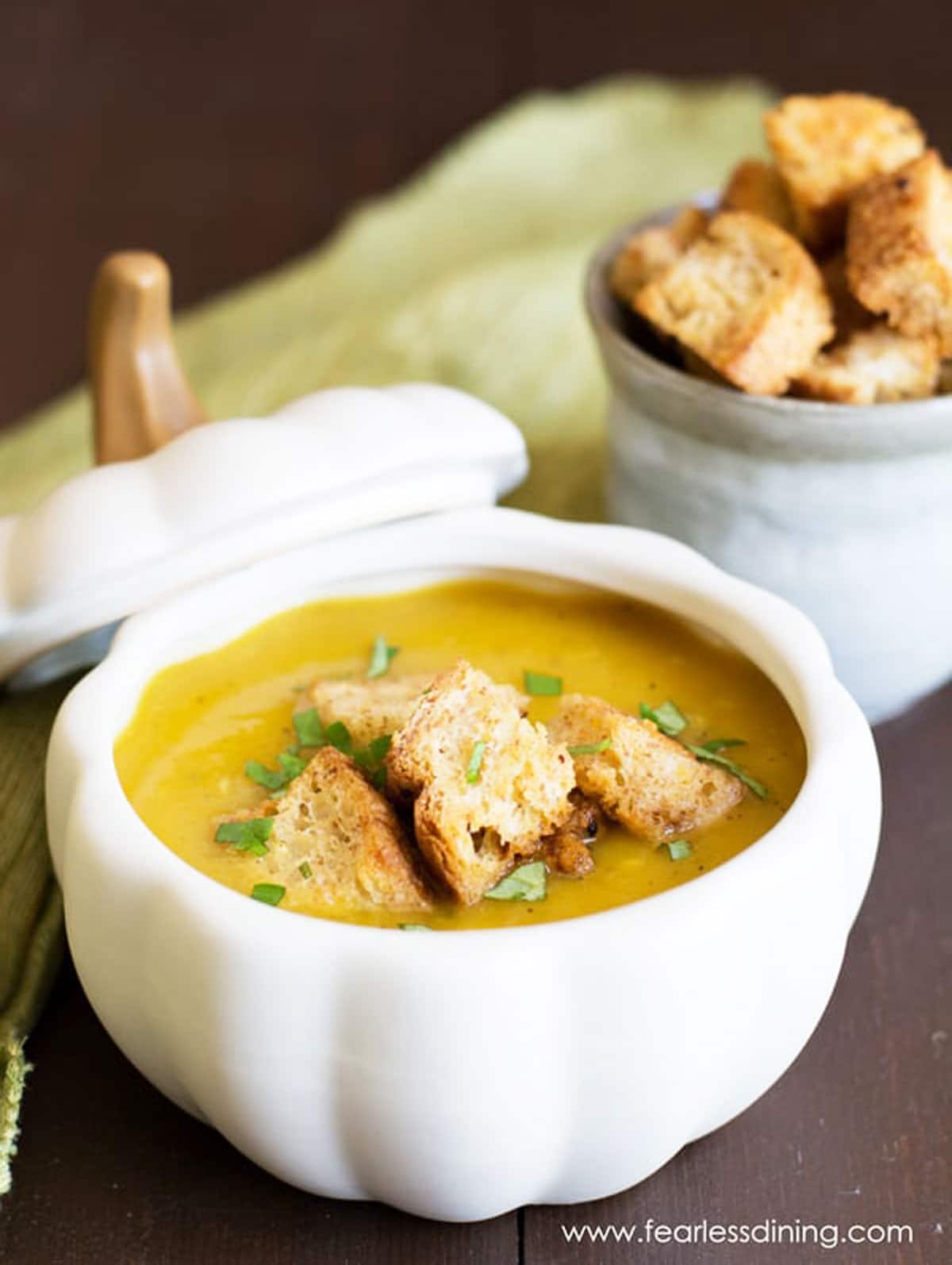 A white squash shaped bowl of roasted acorn squash soup topped with croutons.