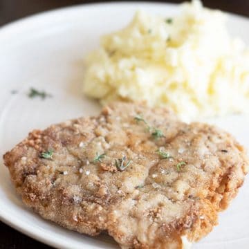 A piece of gluten free chicken fried steak on a plate with mashed potatoes.