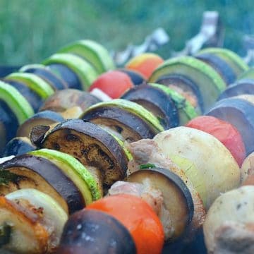 Vegetables on skewers cooking on a grill.