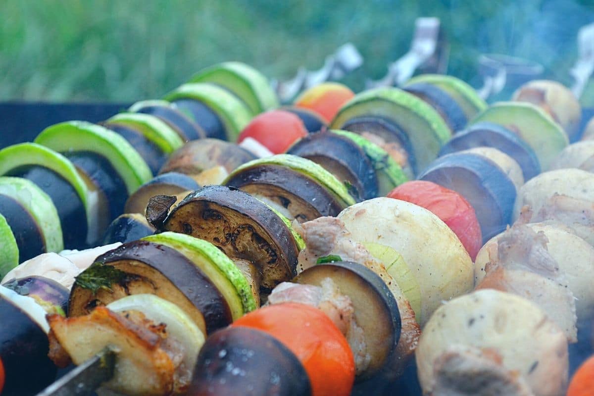 Vegetables on skewers cooking on a grill.