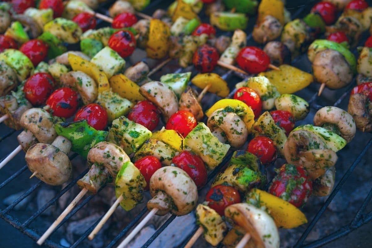 vegetables coated in pesto on skewers cooking on the grill