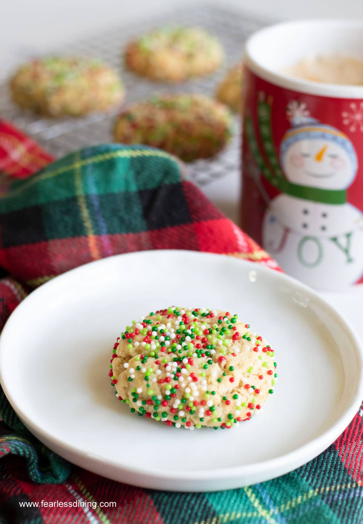 A gluten free cream cheese sugar cookie coated in red and green sprinkles on a plate.