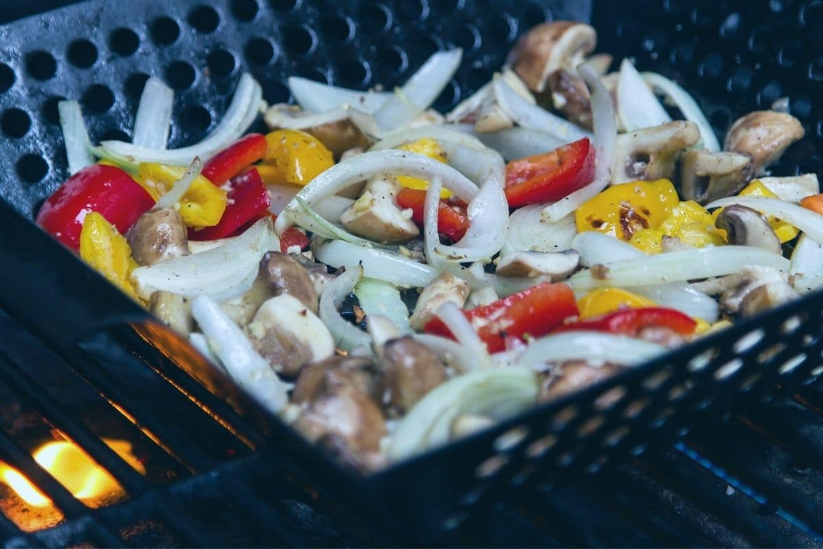 Vegetables in a grill basket cooking on the grill.