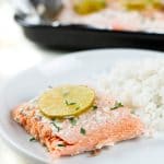 A slice of cooked salmon with rice on a white plate.