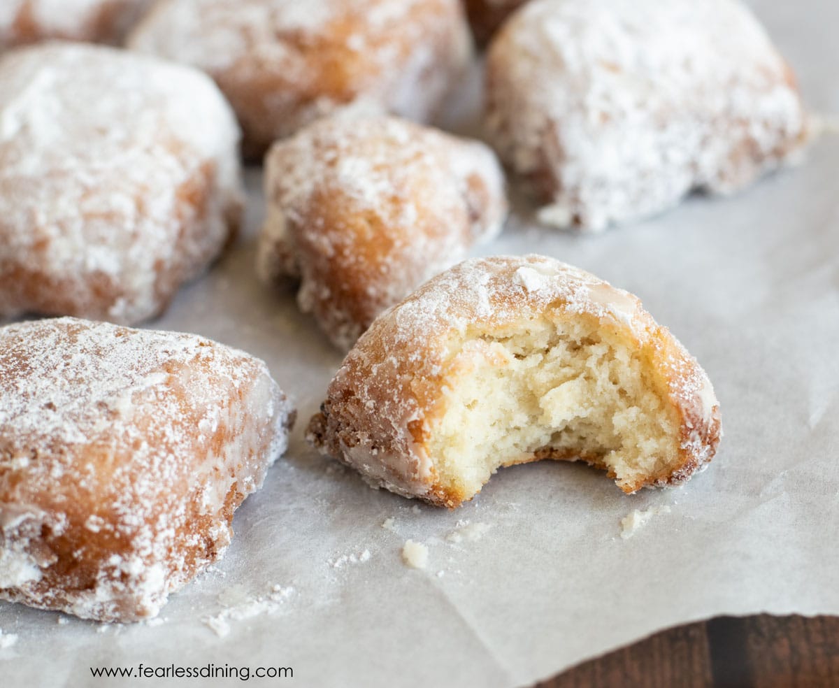 Gluten free beignets on parchment paper. One has a bite taken out.