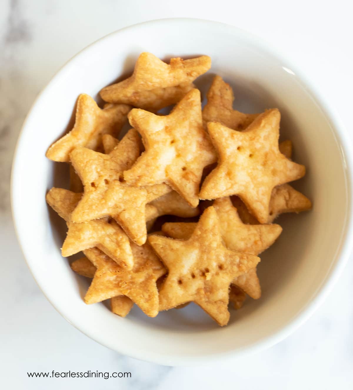 Star shaped gluten free cheez its in a white bowl.