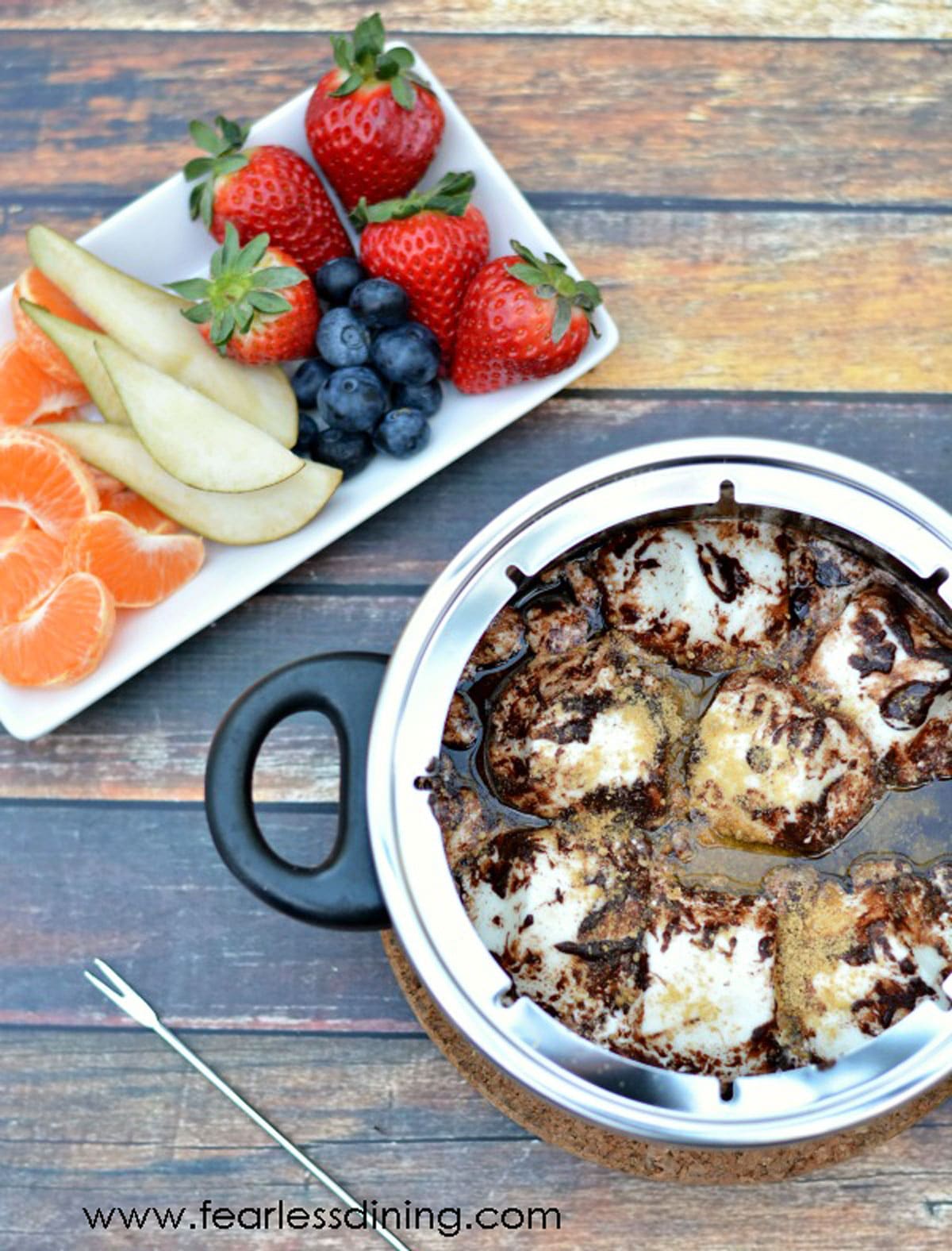 The top view of a fondue pot filled with chocolate fondue next to a fruit plate.