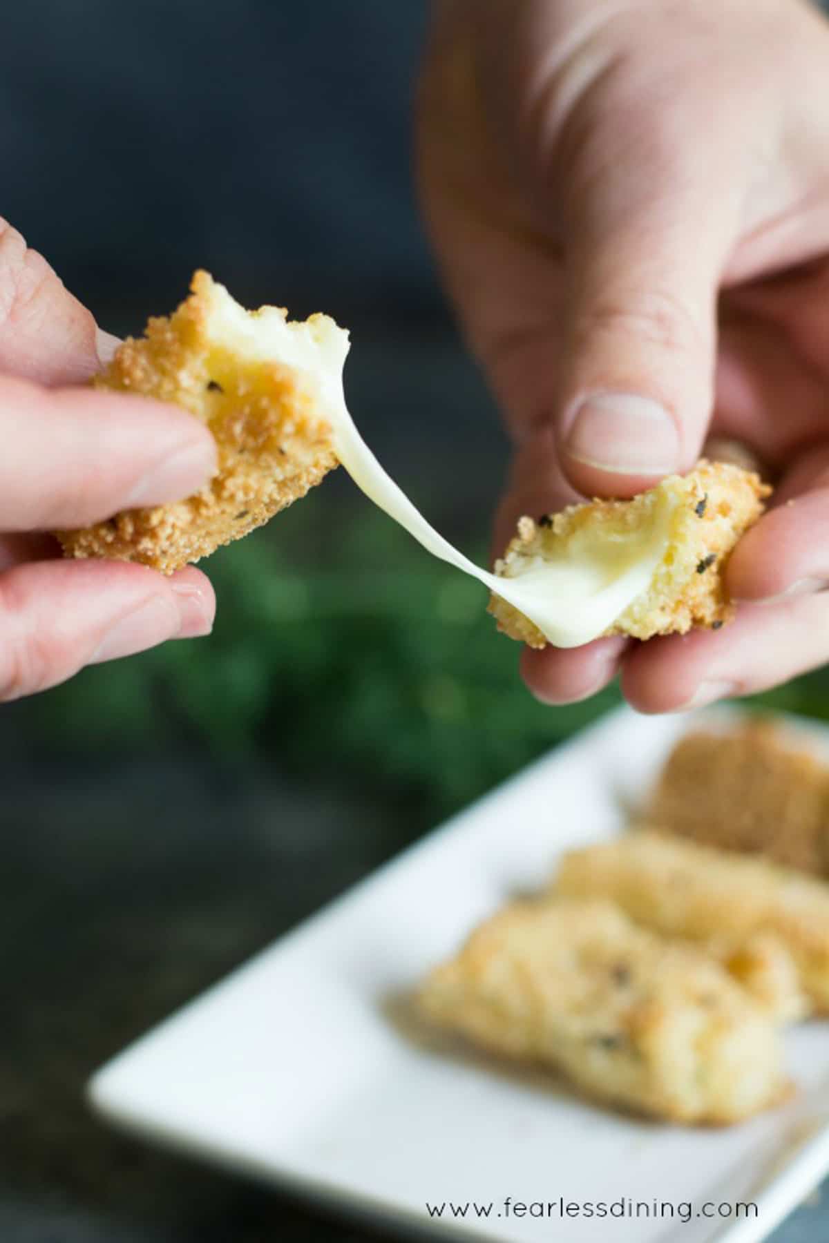 Two hands breaking a hot cheese stick in half.