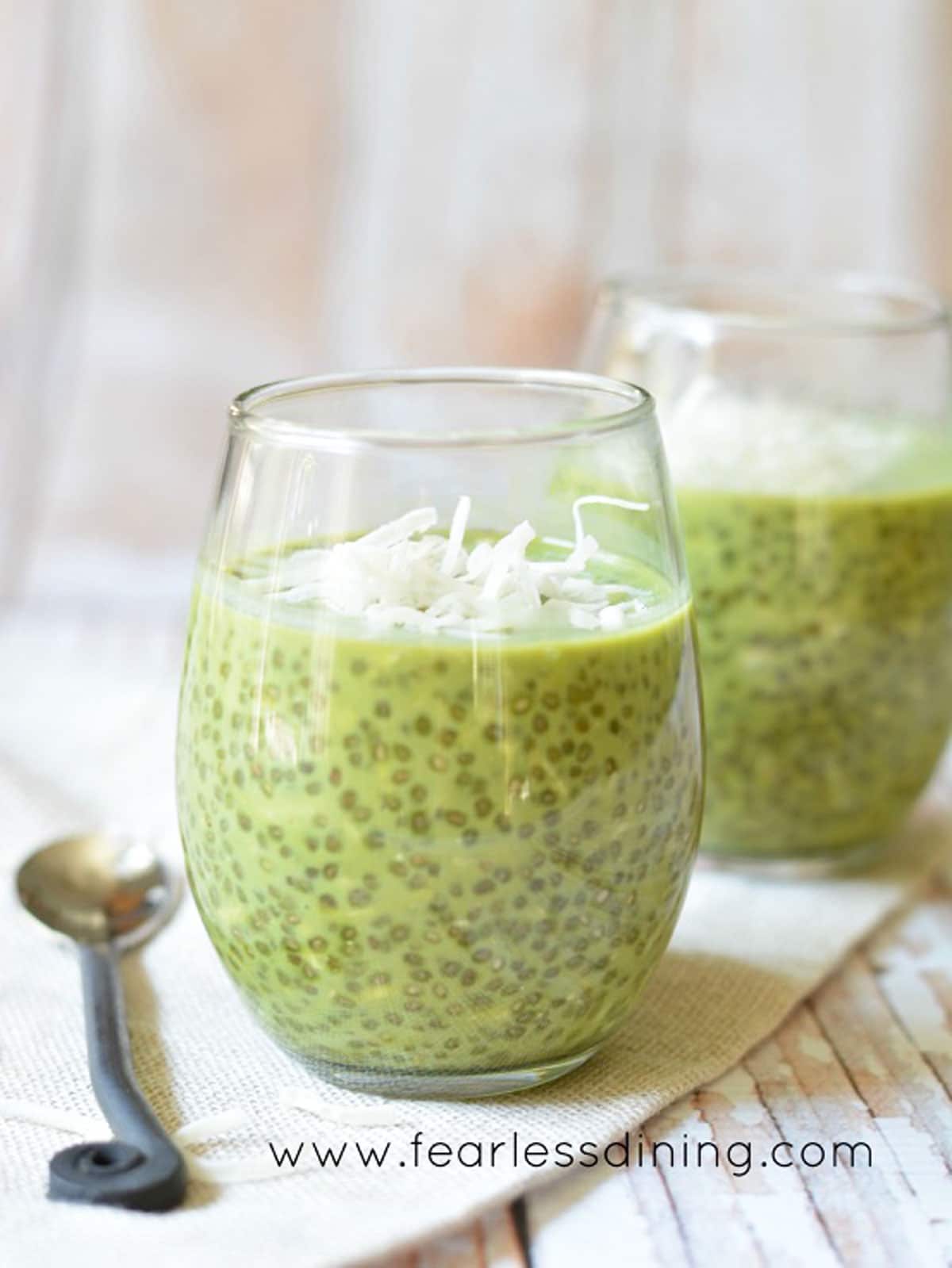 Two wine glasses filled with matcha chia pudding. Each is garnished with shredded coconut.