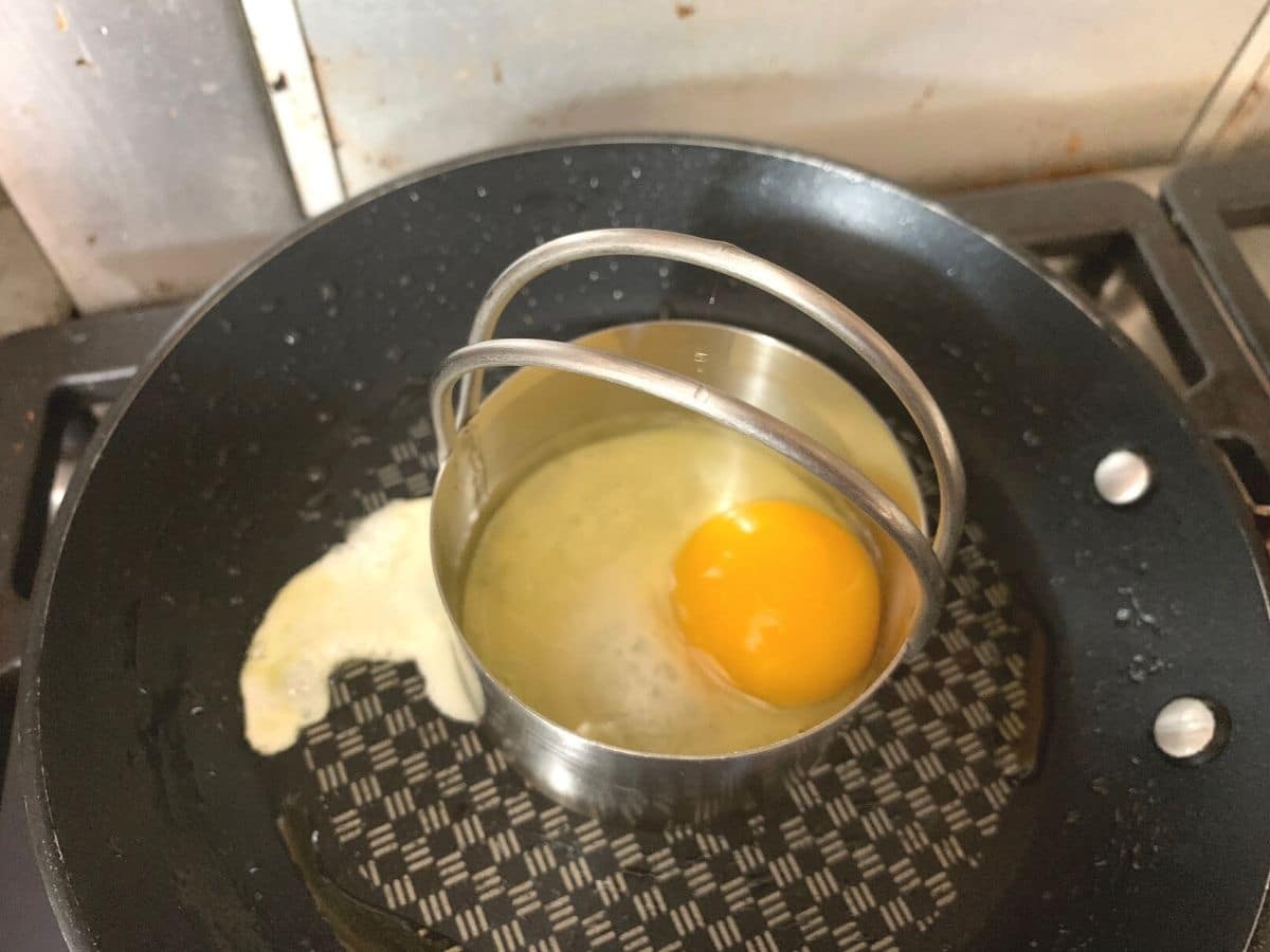 Cooking the egg using a biscuit cutter to hold the shape of the egg.