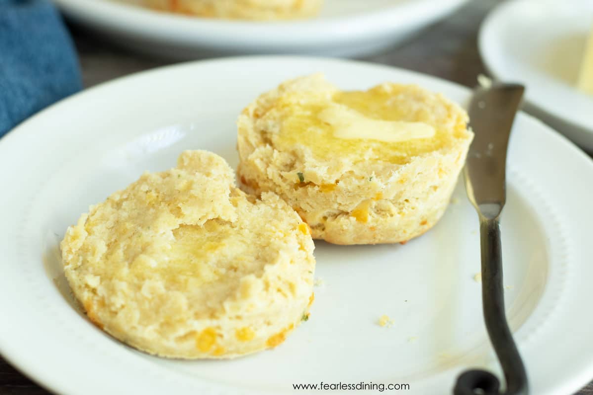 A biscuit sliced in half with butter on a white plate.