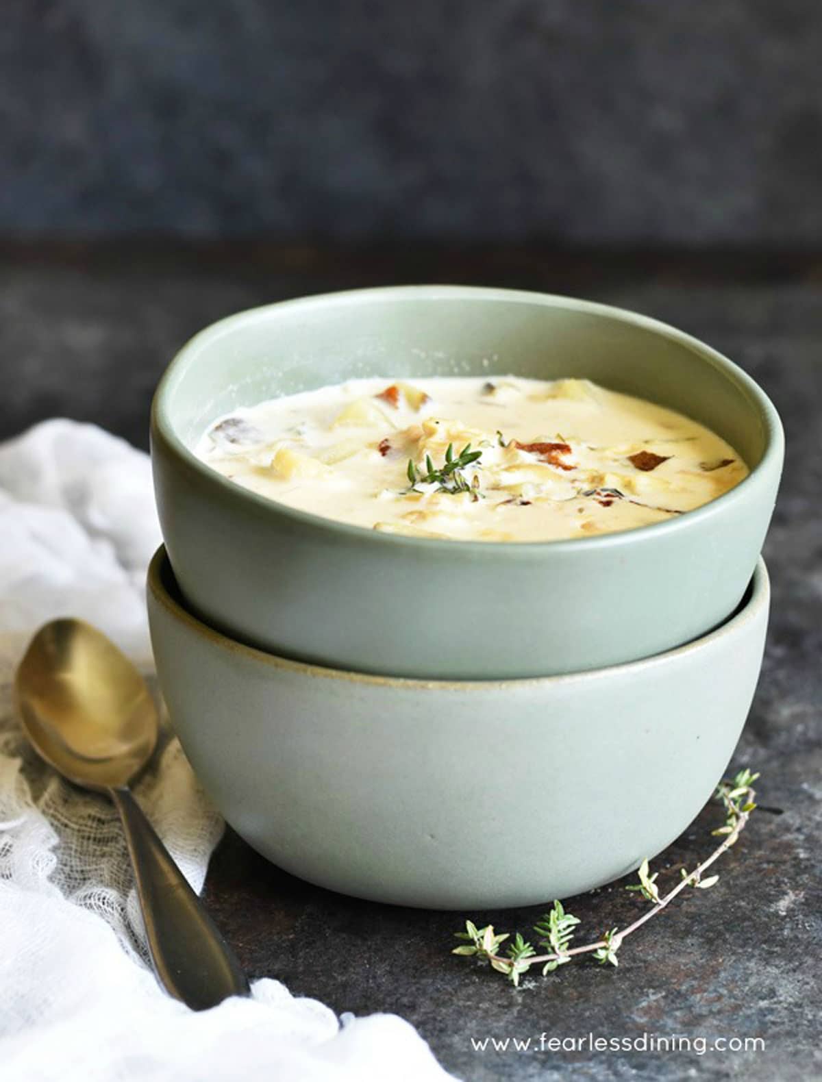 Two sage colored bowls of fish chowder stacked on top of each other.