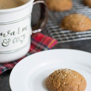 A ginger cookie on a plate next to a mug of coffee.