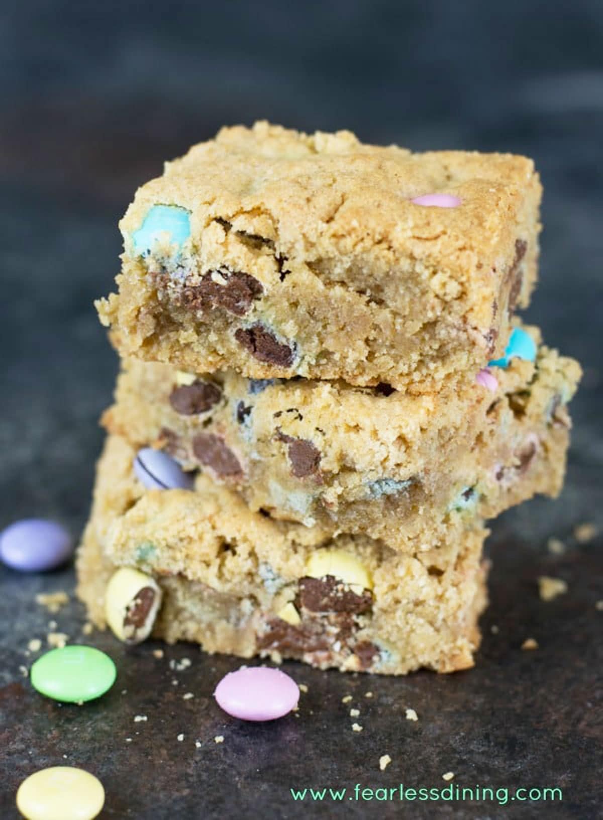 A stack of three peanut butter cookie bars. The bars have pastel M&Ms baked in them.