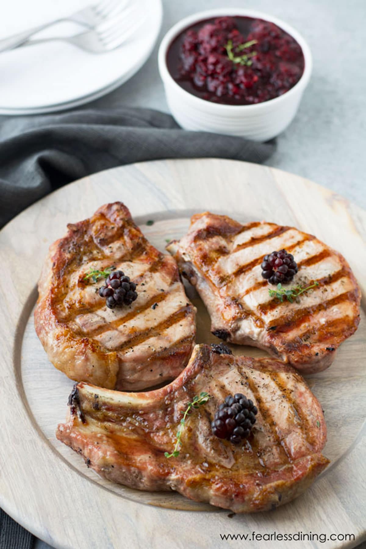 Three rilled pork chops on a wooden plate.