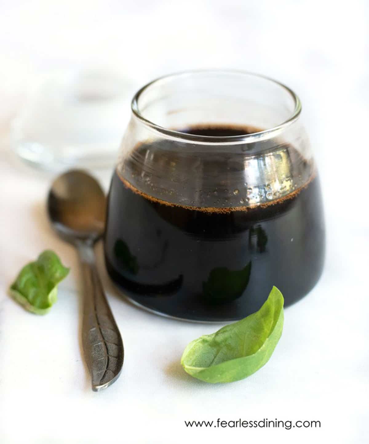 A glass filled with balsamic reduction sauce. A spoon is next to the glass.