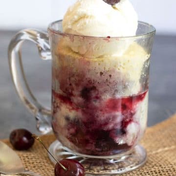 A cherry cobbler in a glass mug topped with ice cream and a fresh cherry.