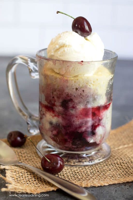A cherry cobbler in a glass mug topped with ice cream and a fresh cherry.
