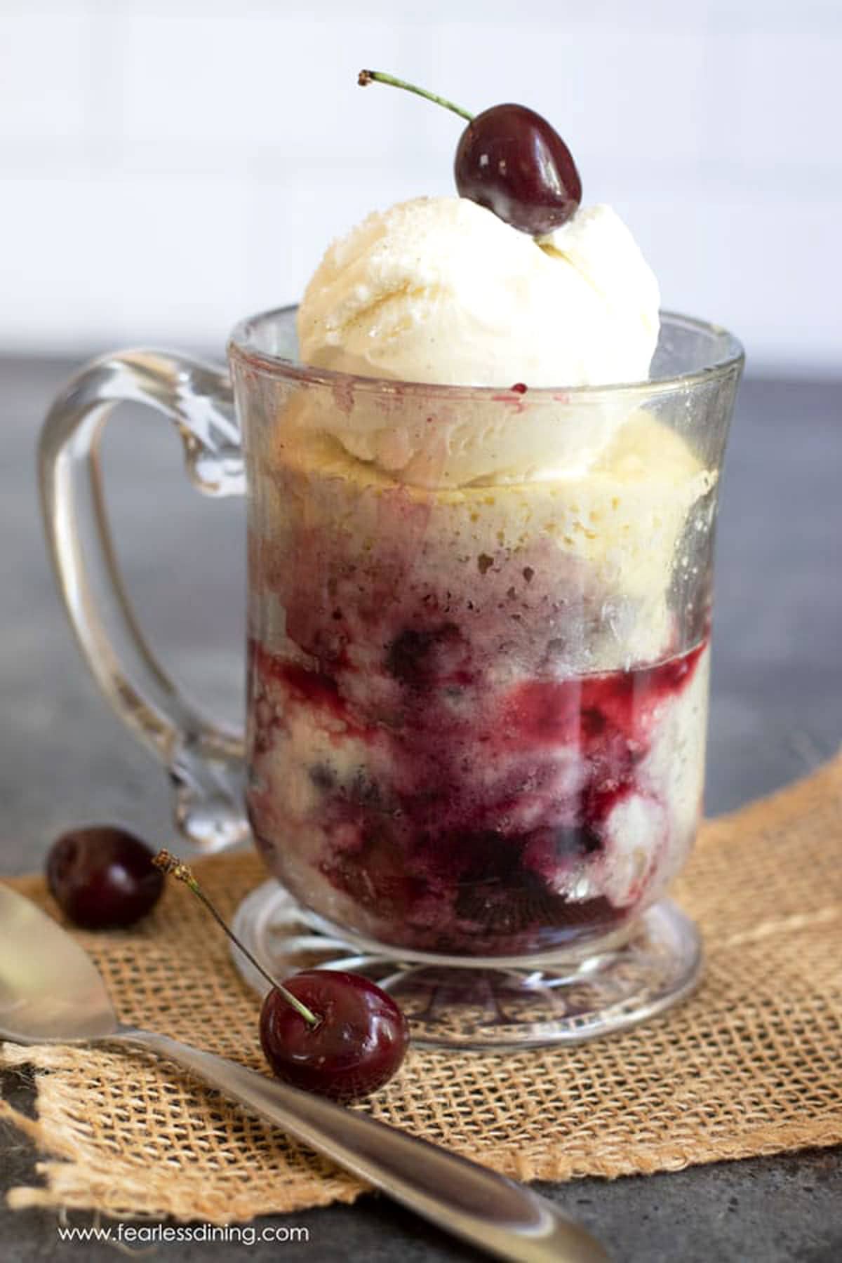 A cherry cobbler in a glass mug topped with ice cream and a fresh cherry.