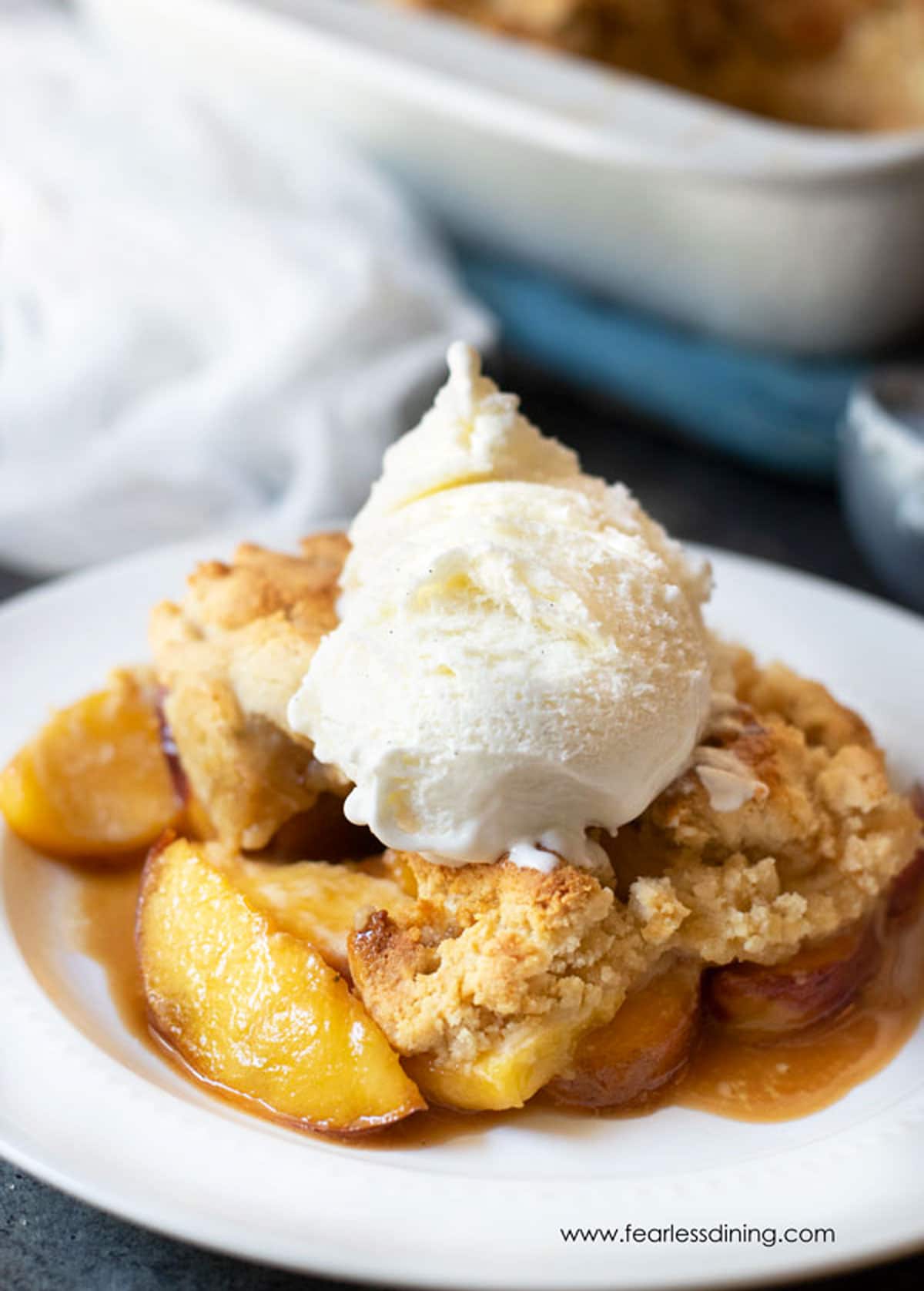 A wide bowl full of peach cobbler topped with ice cream.