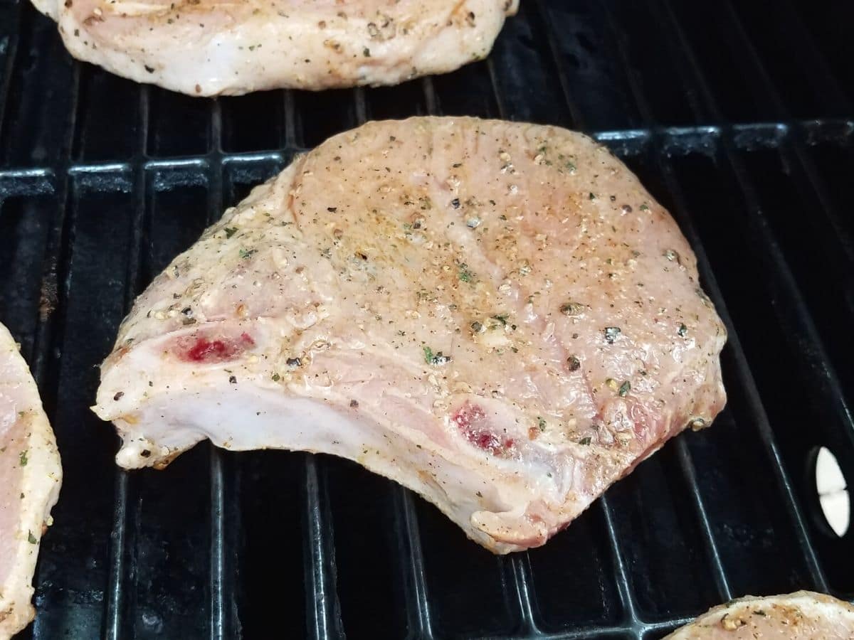 Raw seasoned pork chops on the grill.