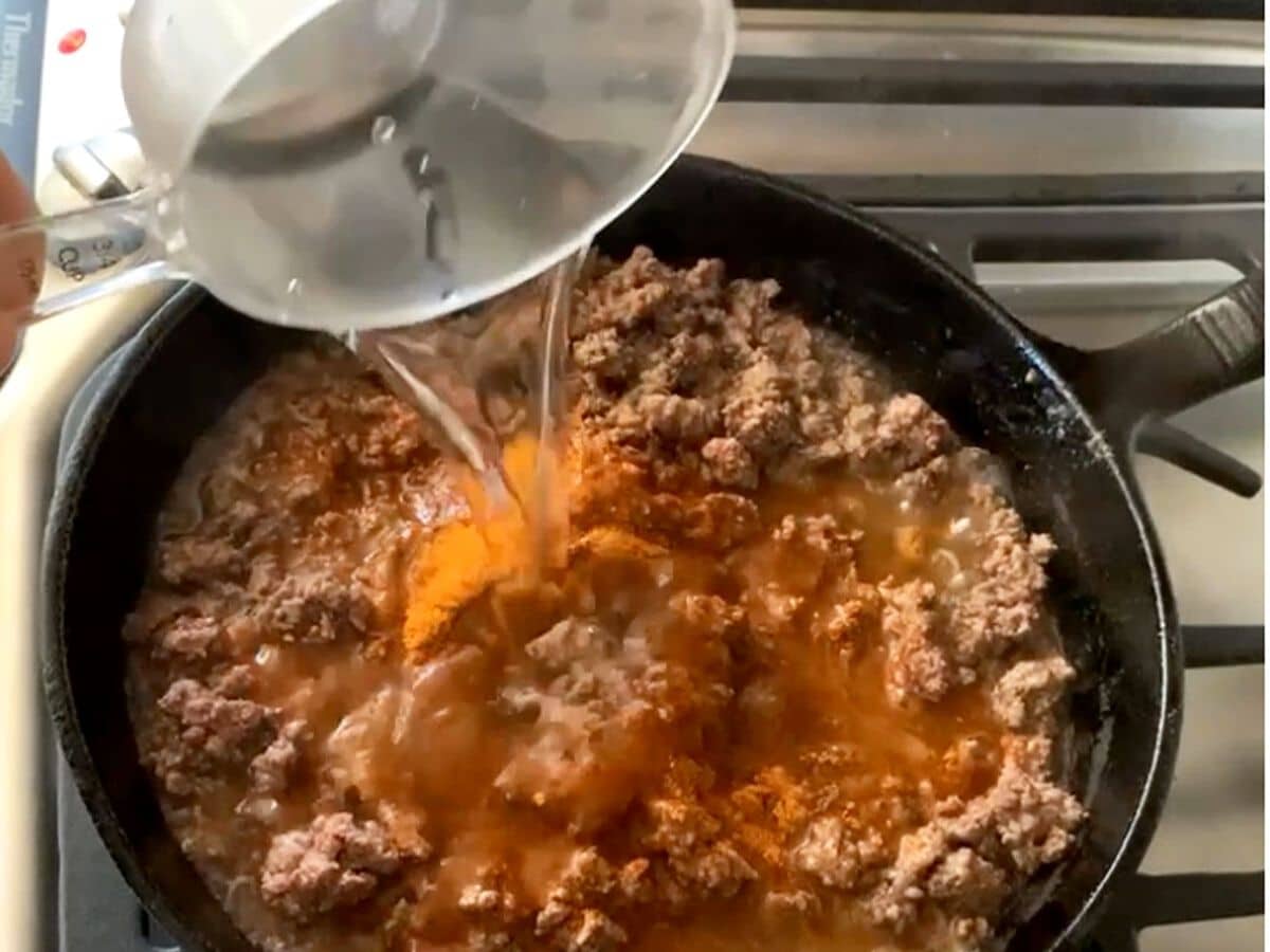 Adding water to the meat and taco mix.
