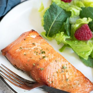 A piece of air fried salmon on a plate with salad.