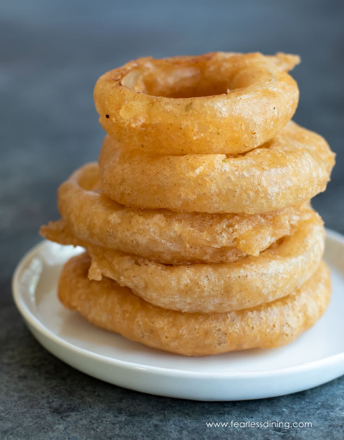 A stack of six large fried onion rings on a plate.