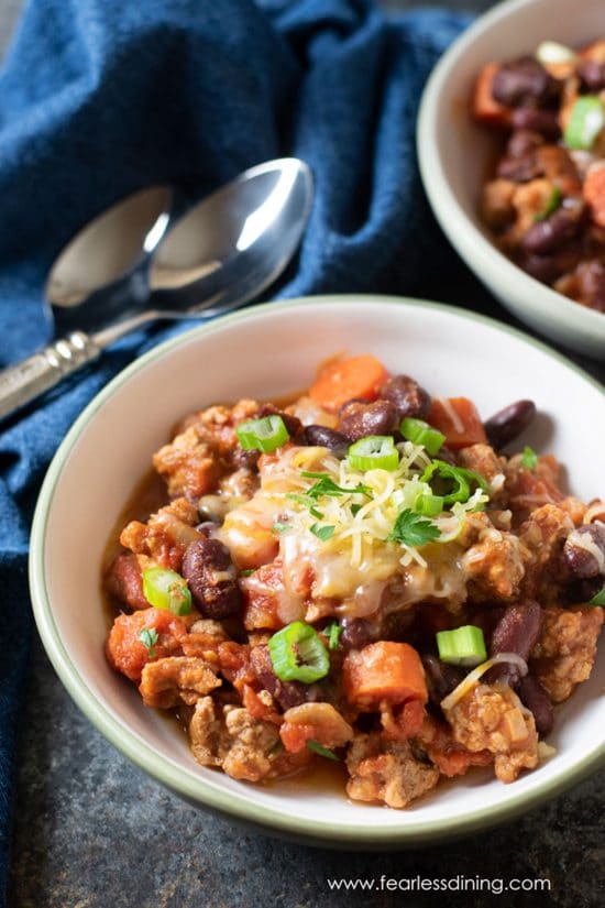 Two bowls full of ground pork chili topped with cheese and scallions.