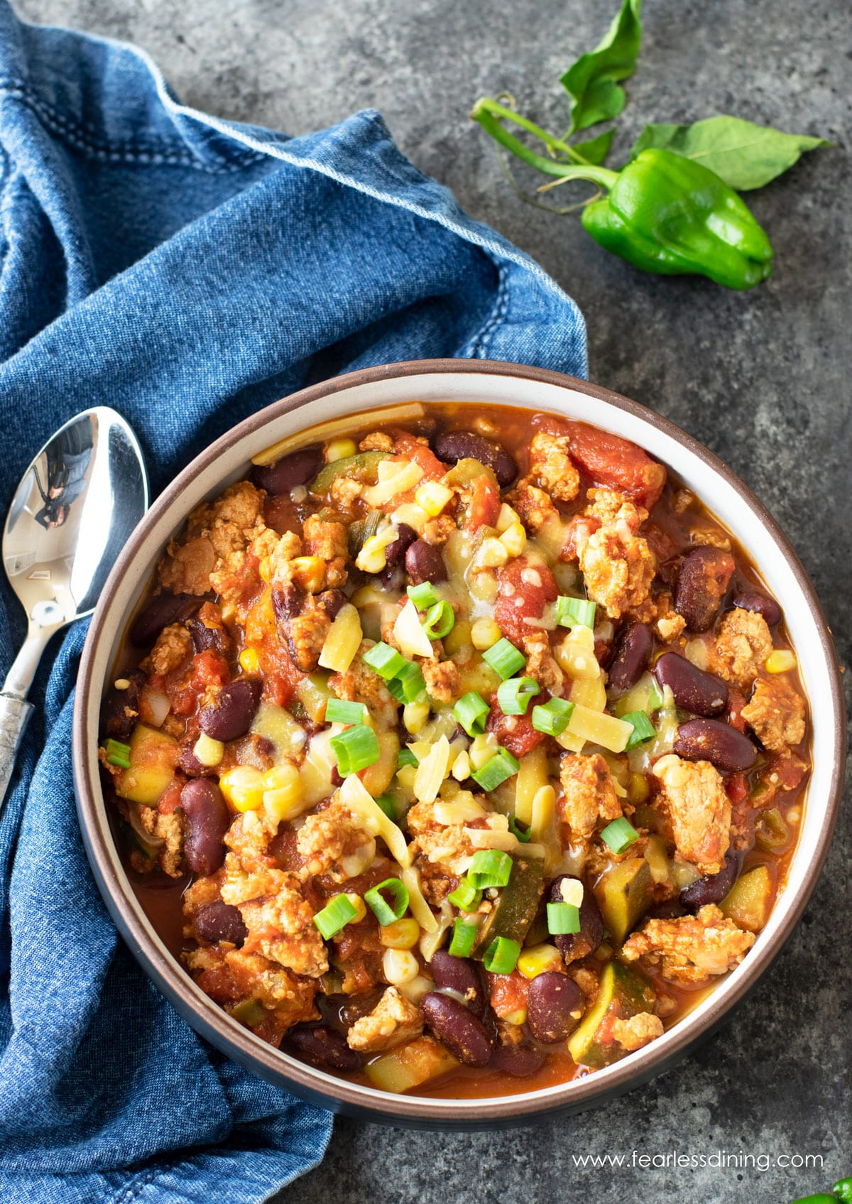 A bowl of padron pepper chili topped with cheese and scallions.