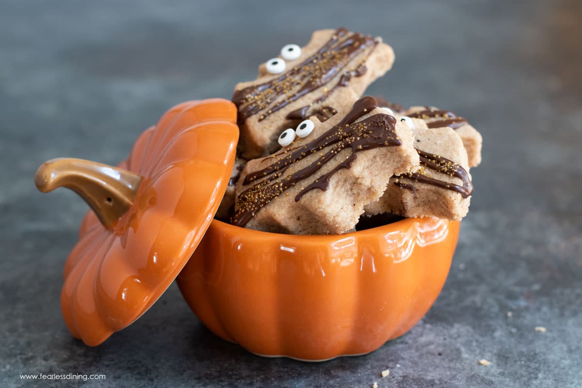 A ceramic pumpkin shaped container filled with pumpkin shortbread cookies.