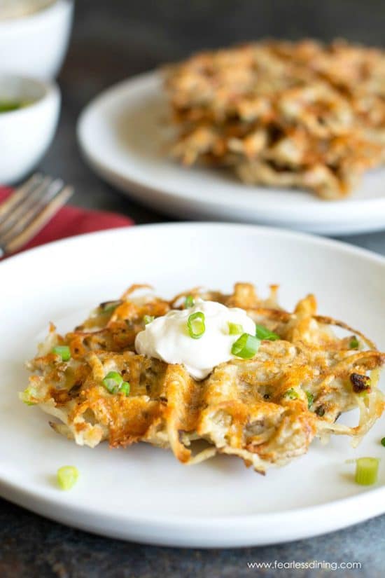 A cheddar waffle iron hash brown on a plate. It is garnished with sour cream and chives.