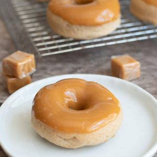 A caramel apple donut on a plate next to a rack of donuts.