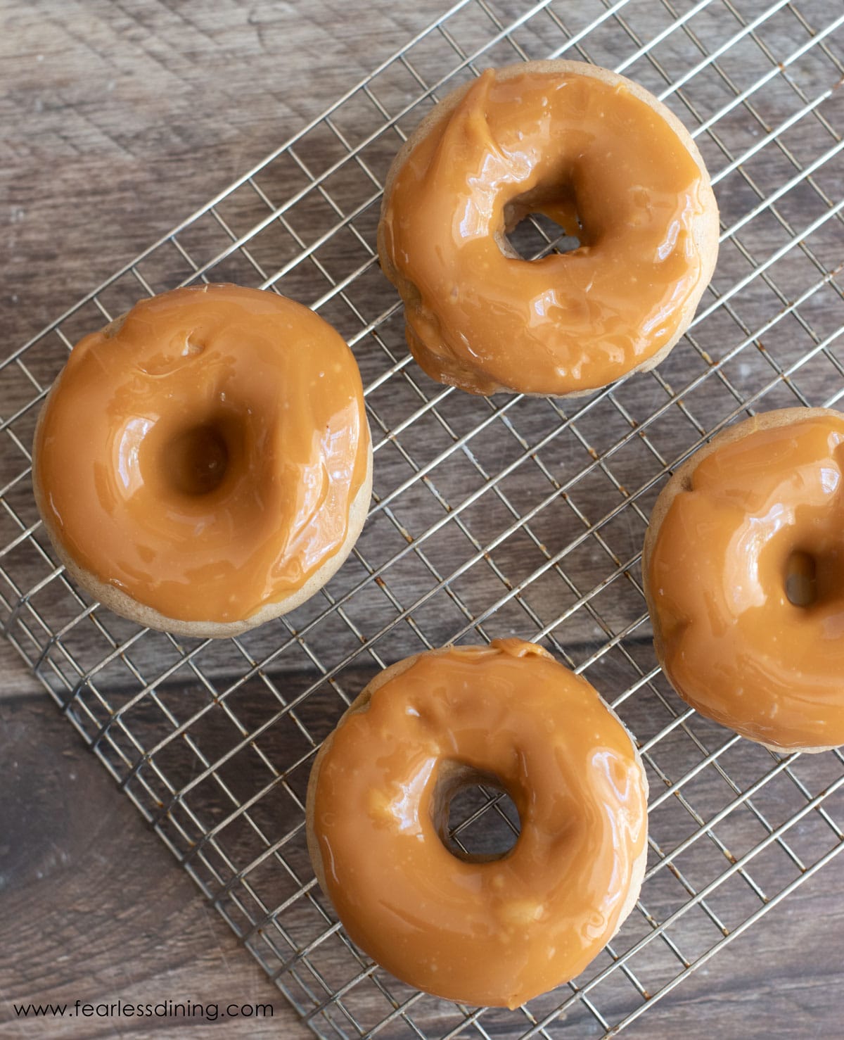 A rack with four caramel apple donuts drying.