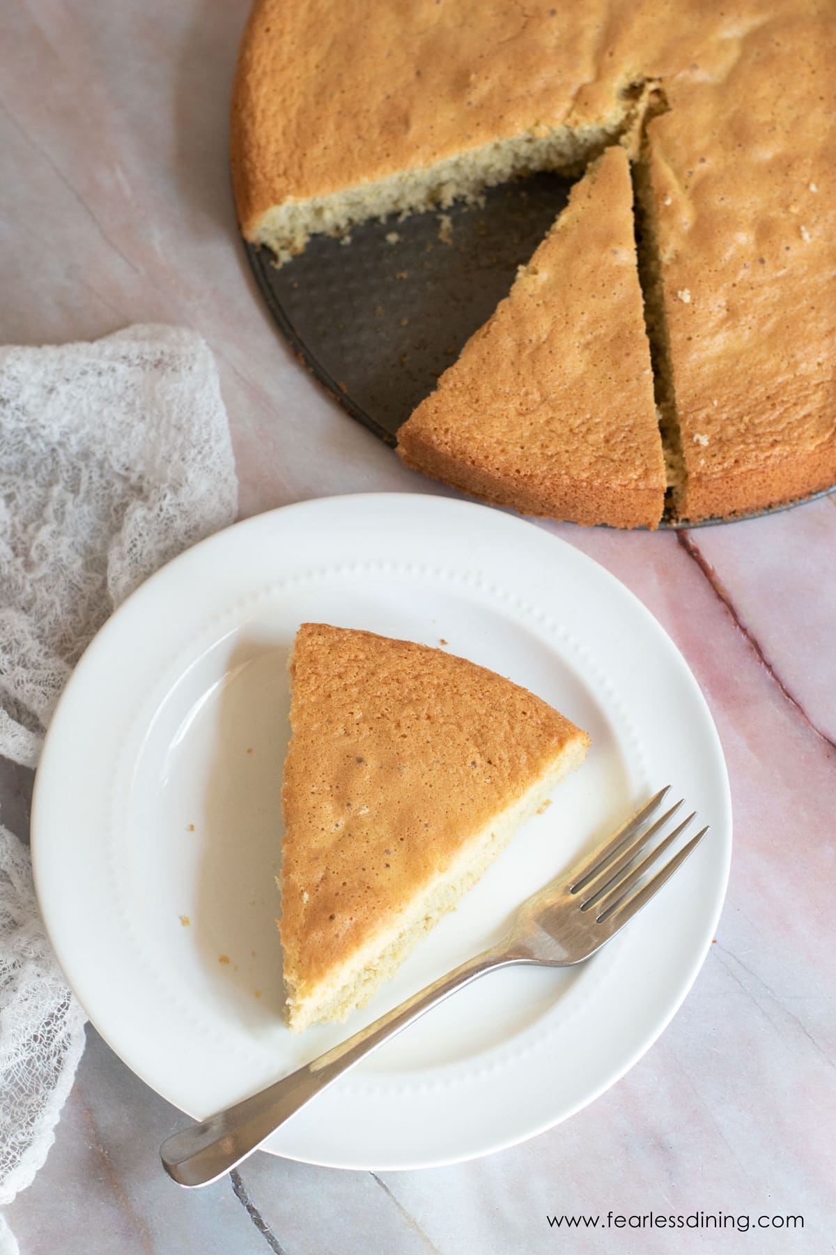 The top view of a slice of sponge cake next to the whole cake.