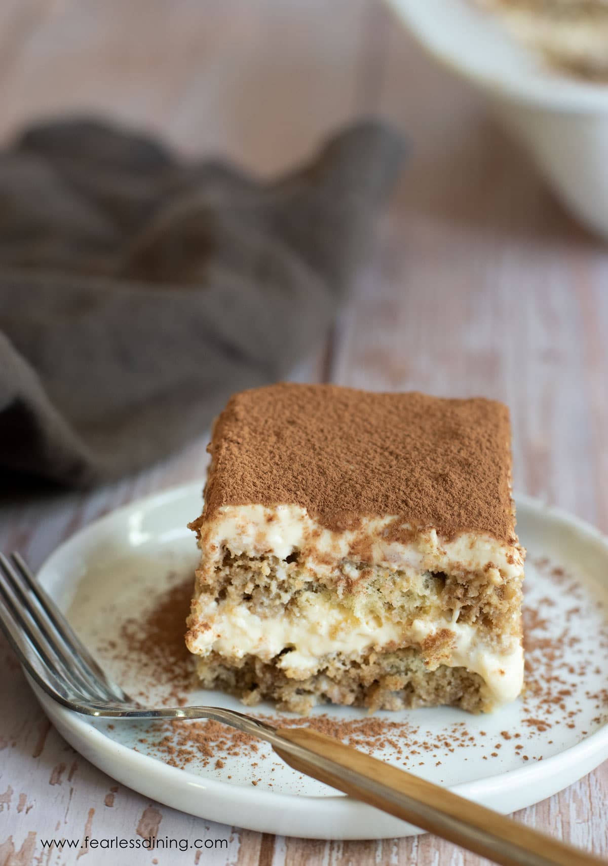 A slice of tiramisu on a plate with a brown fork.