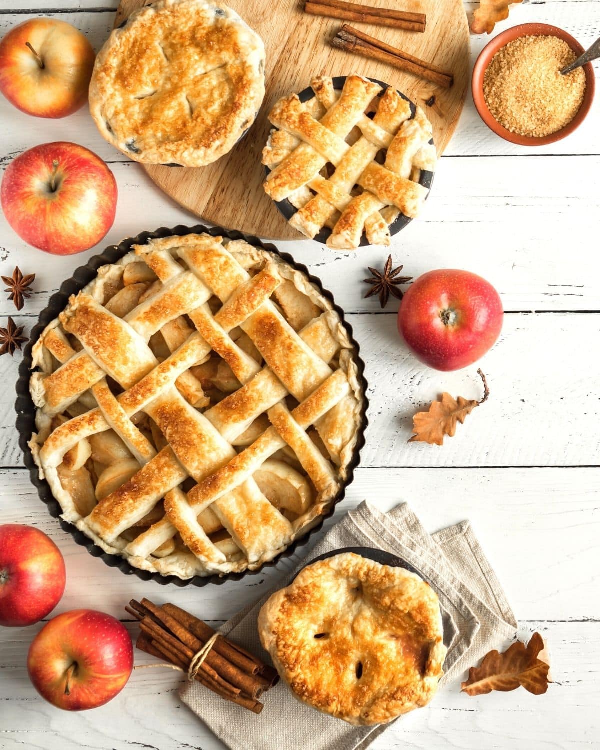 Lots of pies with apples and spices on a table.