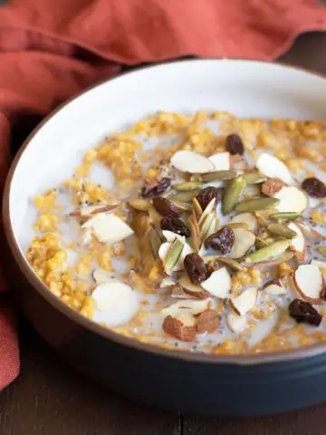a bowl of pumpkin steel cut oats topped with nuts and raisins
