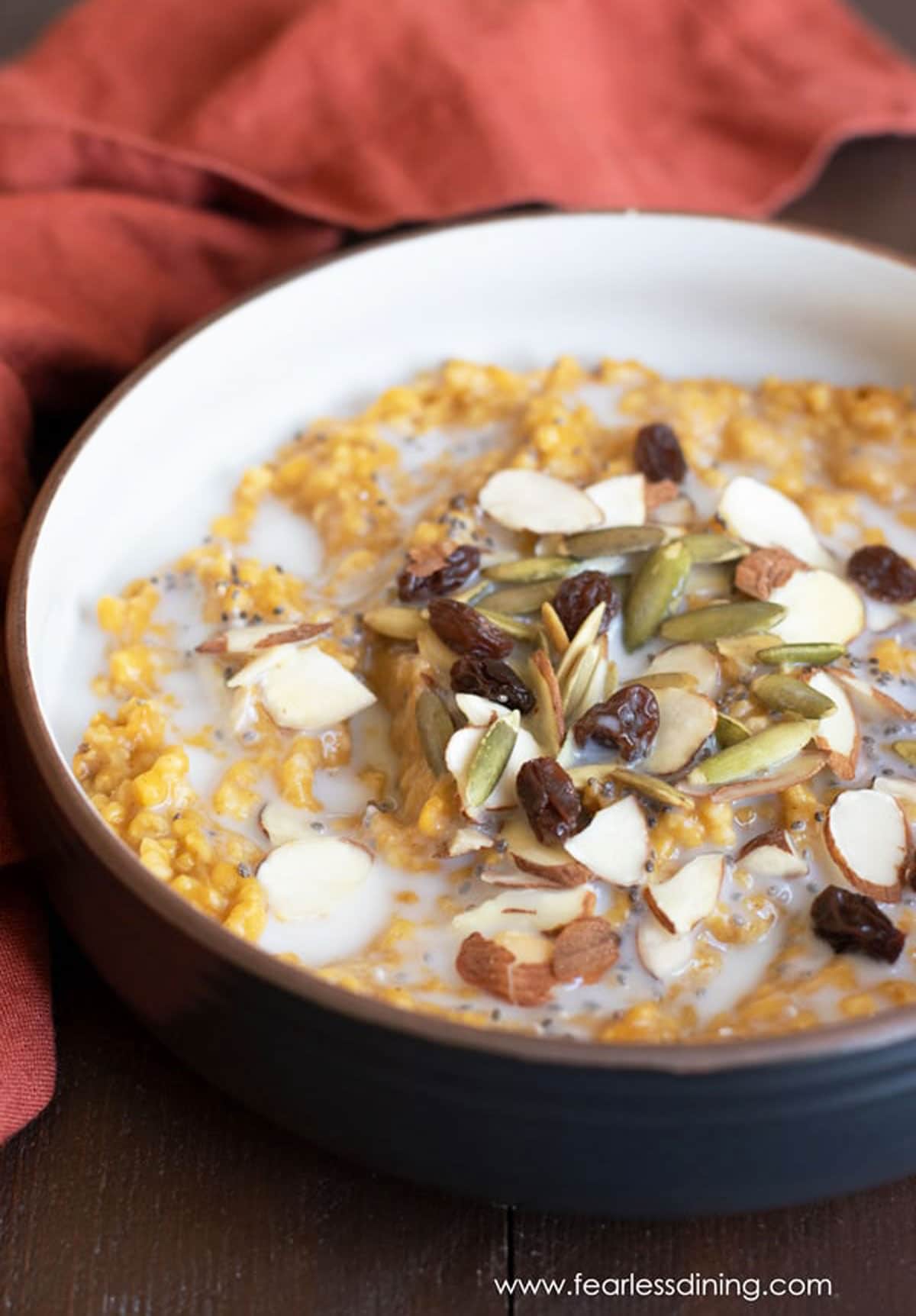 A bowl of pumpkin steel cut oats topped with nuts and raisins.