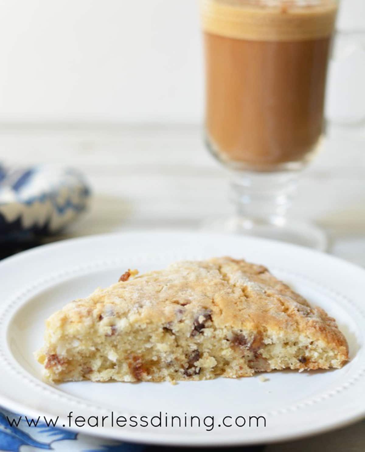 A gluten free date scone on a plate with a latte behind the plate.