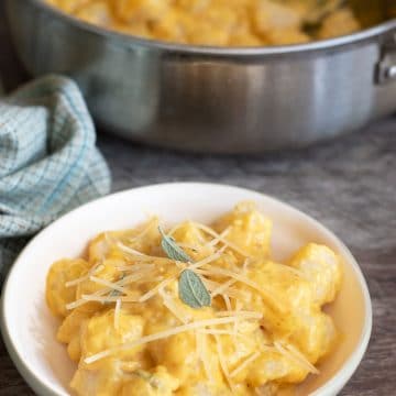 A bowl of gluten free pumpkin gnocchi alfredo. It is next to the pan.