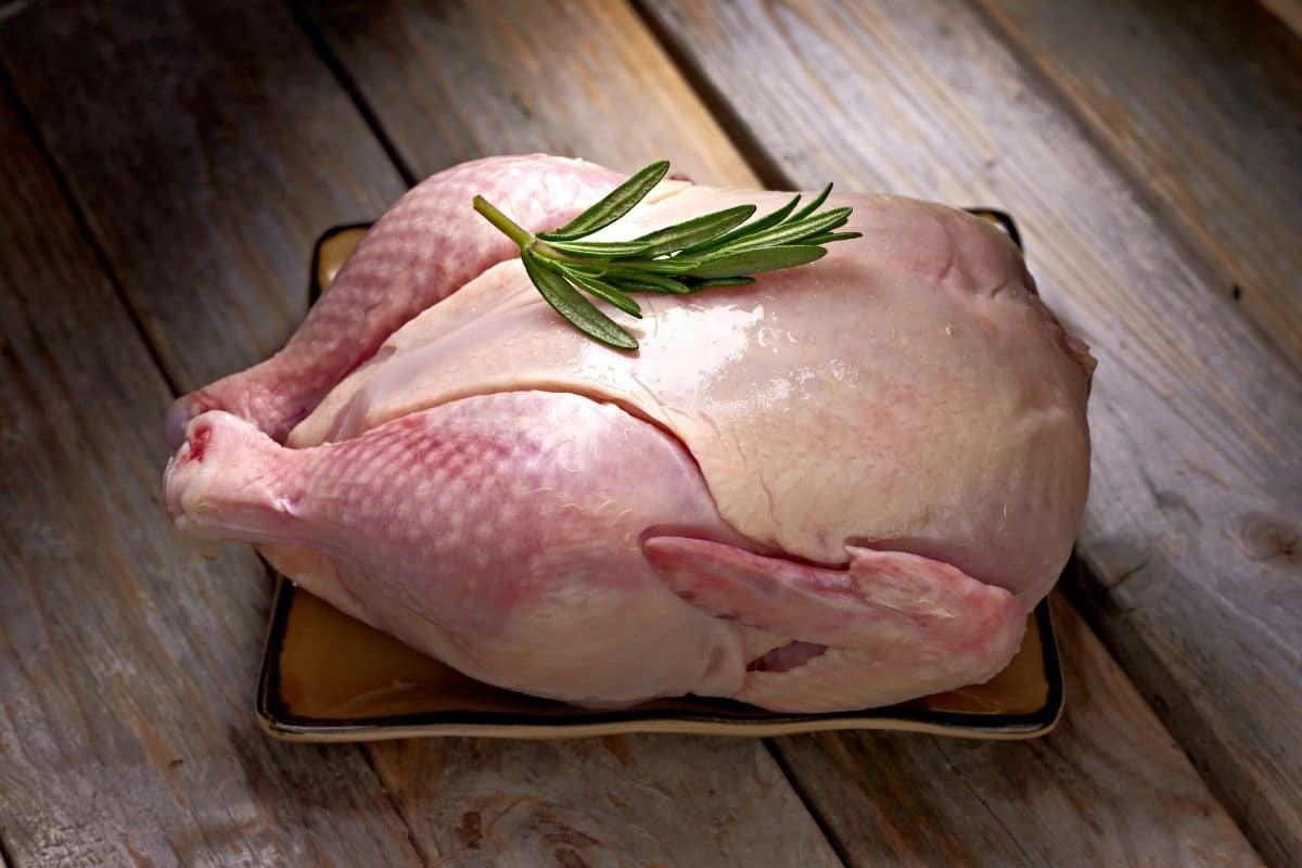 An uncooked cornish hen on a cutting board.