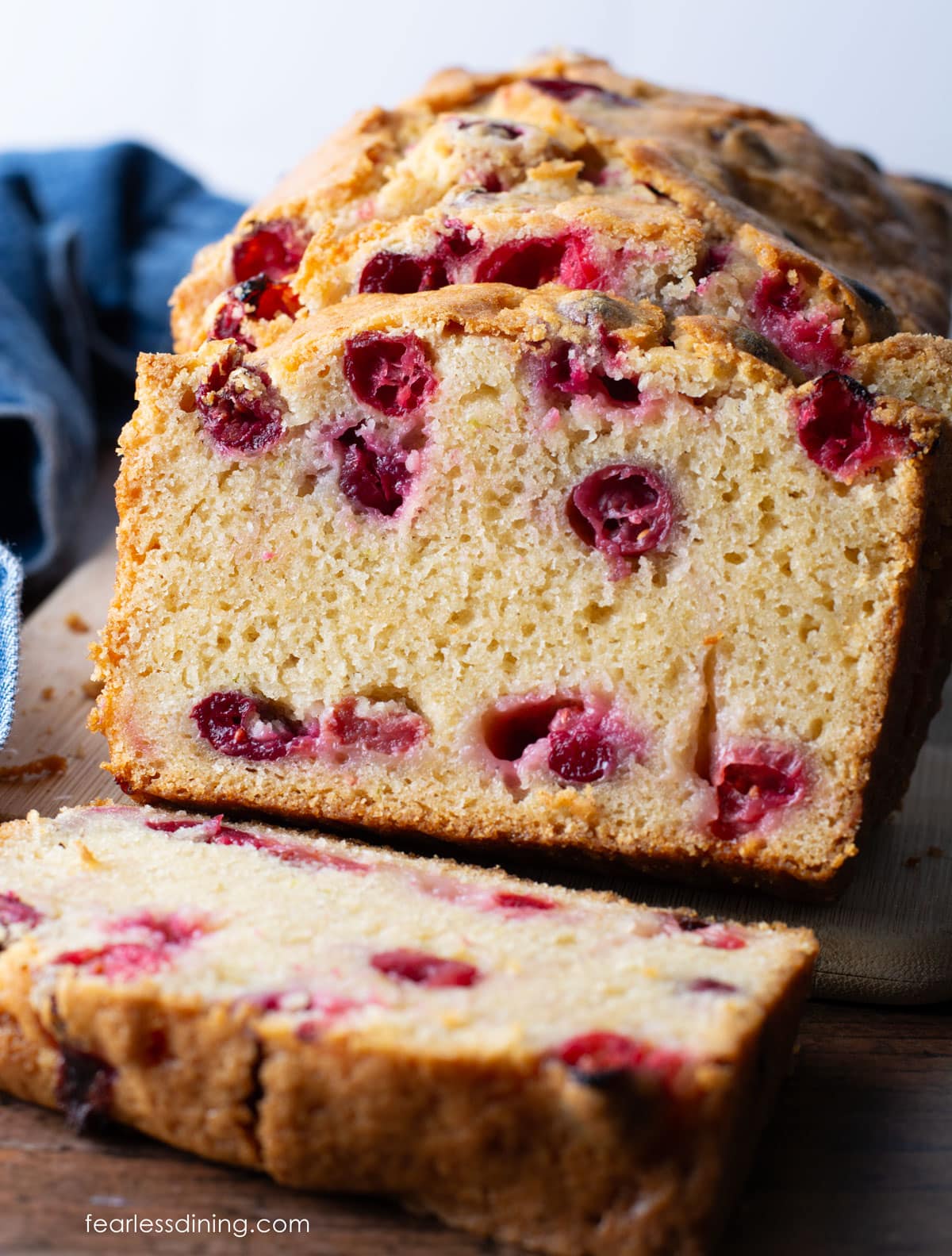 The front view of a sliced gluten-free cranberry pound cake on a wooden cutting board.
