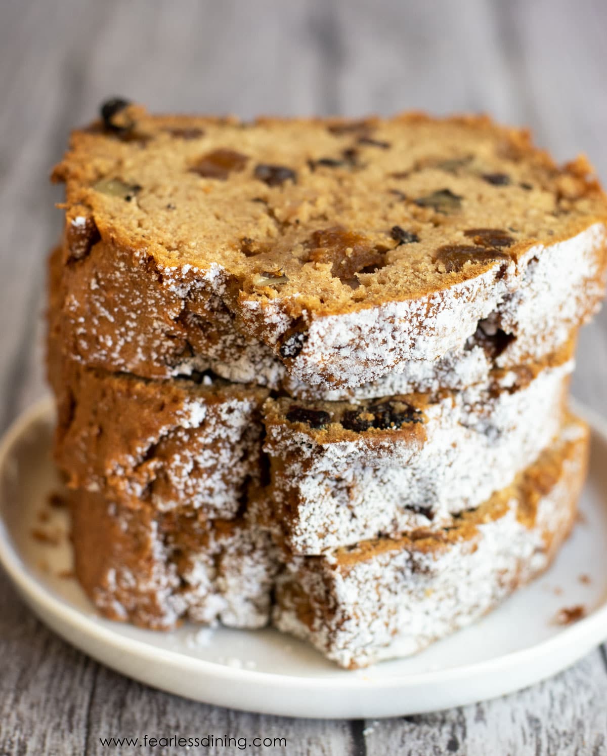 A stack of three slices of gluten free fruit cake on a plate.