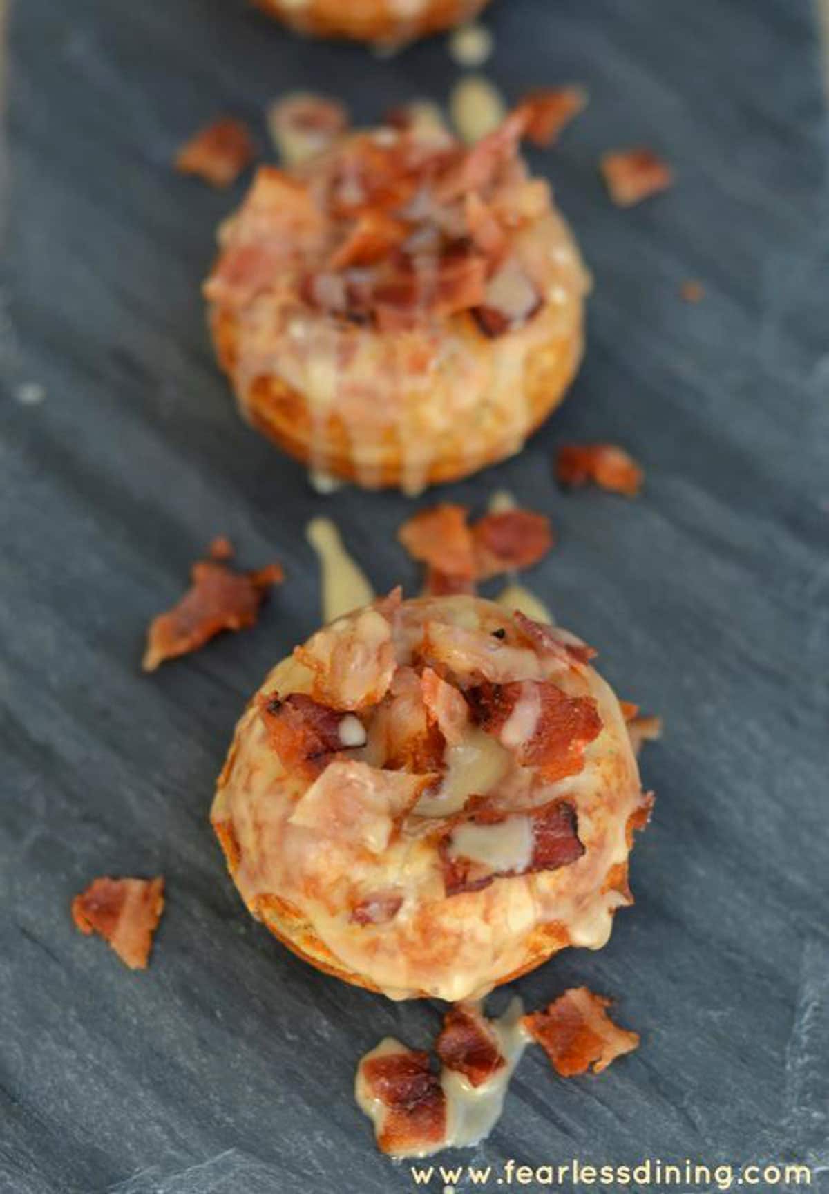 Two maple bacon donuts on a slate serving dish.