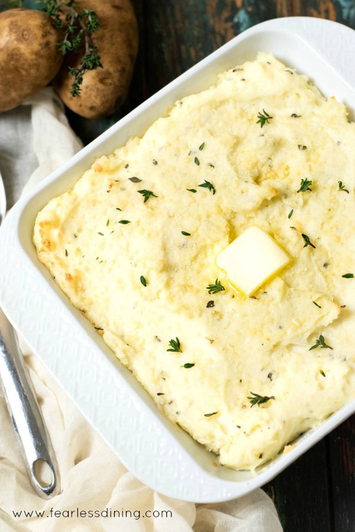 A casserole dish filled with cream cheese mashed potatoes. It has a butter patty melting on top.