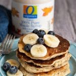 A stack of four gluten free oatmeal pancakes with sliced bananas and blueberries.