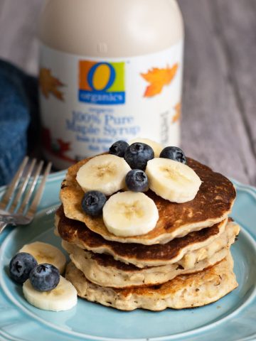 A stack of four gluten free oatmeal pancakes with sliced bananas and blueberries.