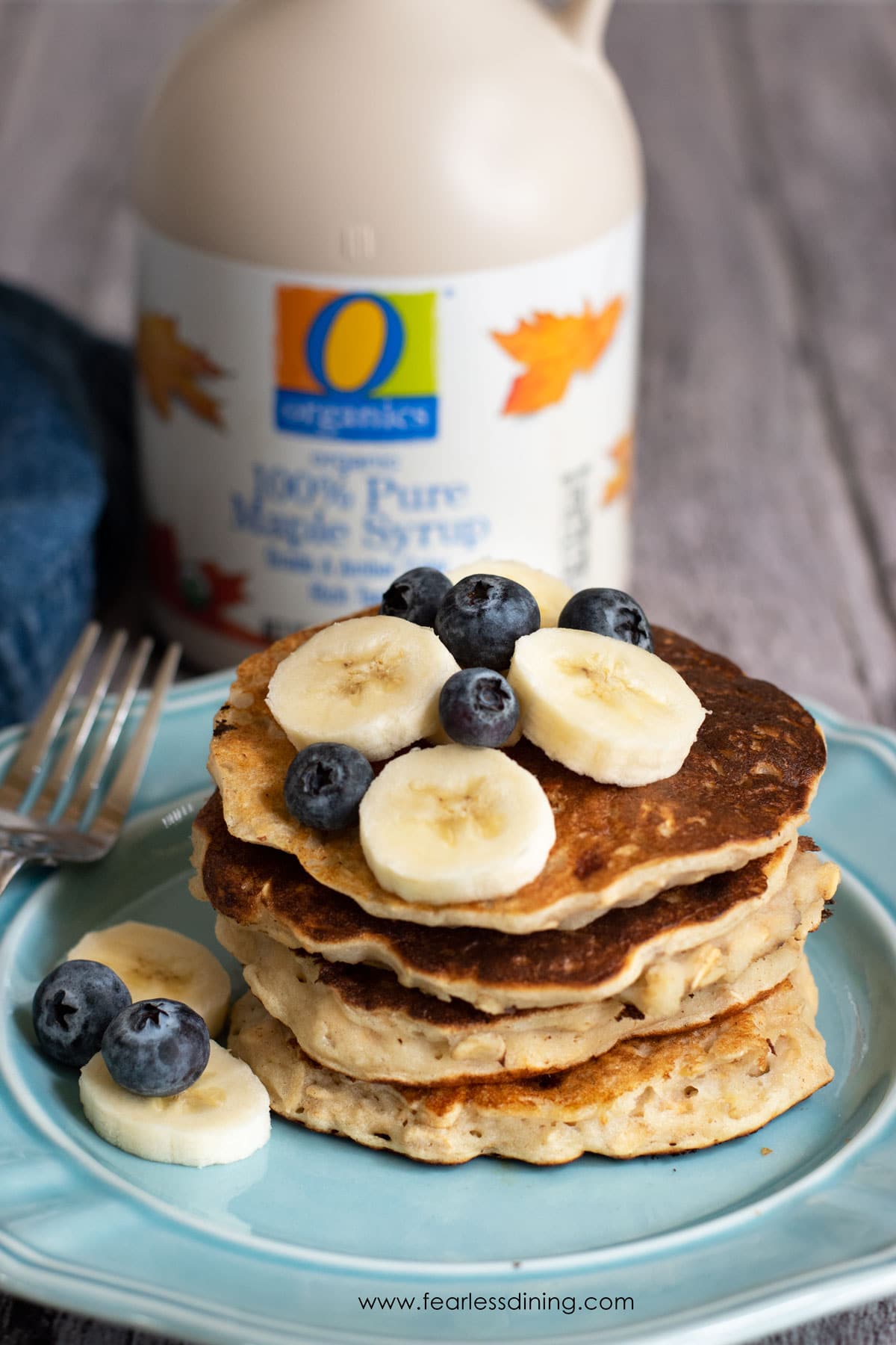 A stack of four gluten free oatmeal pancakes with sliced bananas and blueberries.