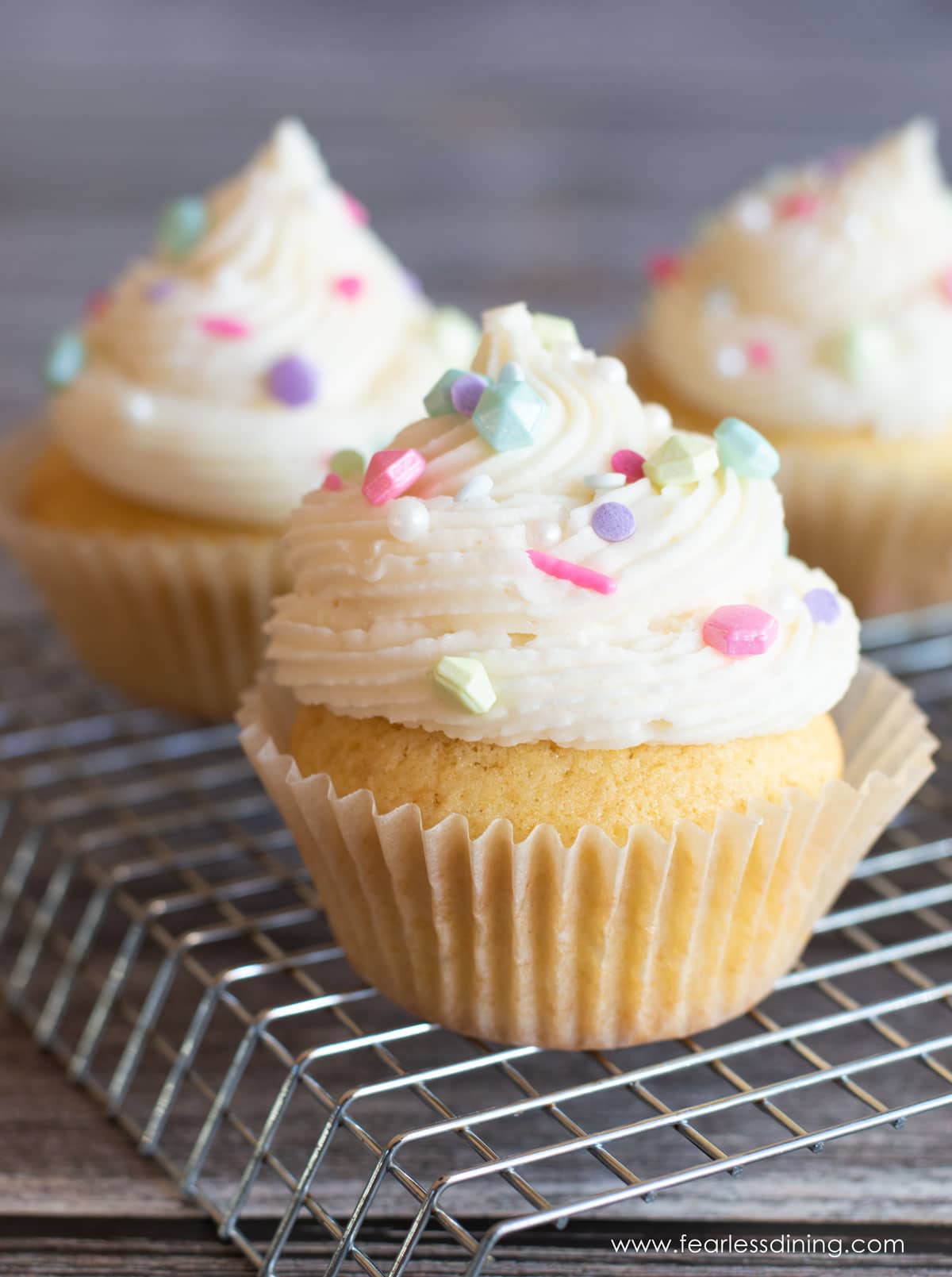 Frosted gluten free vanilla cupcakes on a rack.